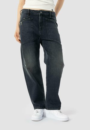 Dark blue denim jeans with a loose fit, visible stitching, and two back pockets. Paired with white sneakers on a neutral background.