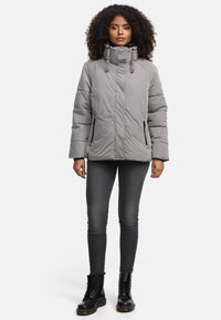Grijze gewatteerde jas met een hoge kraag, zijzakken en verstelbare trekkoorden. Combinatie met donkere jeans en zwarte veterschoenen.