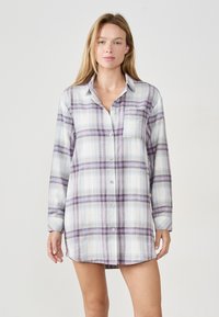 Koszula w kratę zapinana na guziki wykonana z miękkiego materiału, w odcieniach fioletu i niebieskiego, z długimi rękawami, kołnierzykiem i kieszonką na piersi. Dół koszuli sięga do połowy uda.