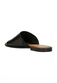 Sandale en cuir noir, à bout ouvert et sans arrière. Dispose d'une semelle plate et d'une texture lisse avec un minimum de détails de couture.