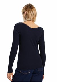 Marine ribbed pitkähiha T-paita, jossa on V-muotoinen kaula-aukko, tiukka muotoilu ja hienovarainen teksturoitu viimeistely. Helma ulottuu lantion tasolle.