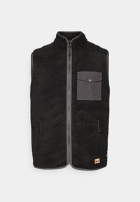 Svart fleece uten ermer med glidelås foran, grå klaff brystlomme, to glidelåslommer på siden, og liten logo-patch nederst.