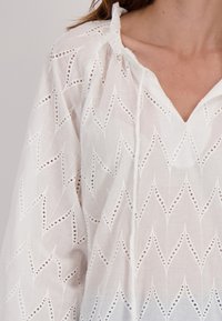 Witte blouse met een V-hals, voorzien van ingewikkelde uitsnijdpatronen en een gestructureerde stof. Losse pasvorm met een gathered halslijn.