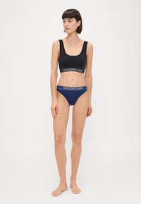 Svart bralette med logo-livrem, kombinert med marineblå bikini-truser med en kontrast-logo-bånd, begge laget av elastisk stoff.