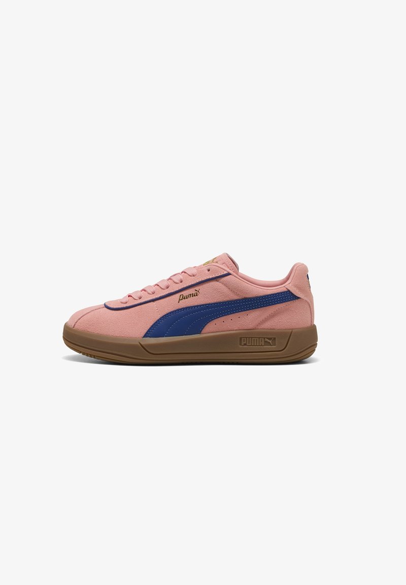 Puma sneakers in pink suede with a blue stripe, featuring a brown rubber sole, rounded toe, and flat laces. Gold logo detail on the side.