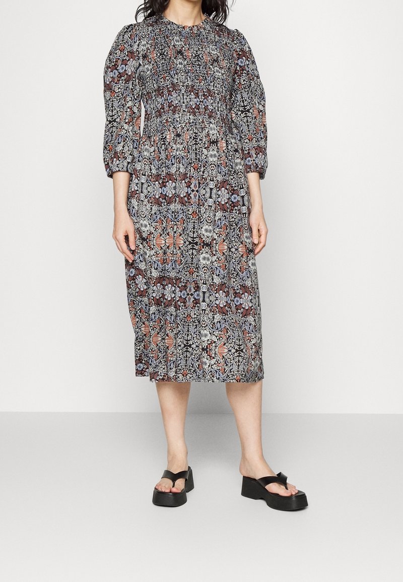 Kukkakuosisessa mekossa on laskostettu kaula-aukko, kolmanneksen pituiset hihat ja kyynärpäihin saakka ulottuva pituus. Päävärit ovat musta, punainen ja sininen. Mekko on yhdistetty paksupohjaisiin mustiin sandaaleihin.