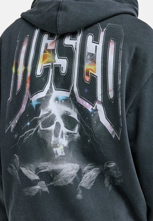 Schwarzer Hoodie mit einem großen, bunten Motiv eines Schädels mit Blitzen, großen "DC"-Schriftzug und Felsformationen. Weicher Baumwollmischstoff.