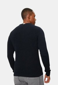 Maglione a coste di colore blu navy con maniche lunghe e scollatura a girocollo. Presenta una maglia testurizzata e un accento a righe in contrasto sul retro.