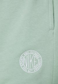 Zelené bavlněné tepláky s výšivkou kruhového loga "NIKE" a "THE SPORTS AND FITNESS COMPANY" v bílé barvě. Měkká textura, uvolněný střih.