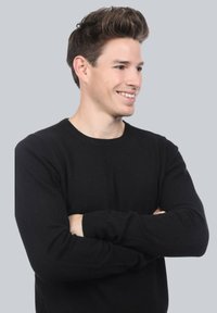 Pull en tricot noir avec des manches longues, un col rond et une coupe ajustée, présenté sur un fond gris clair.