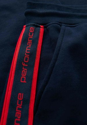 Tissu bleu foncé avec une rayure rouge verticale comportant le mot "performance" cousu à plusieurs reprises en fil rouge.
