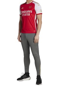 Red and white soccer jersey with "Emirates Fly Better" branding, paired with gray fitted pants. Includes gold accent stripes. Black sneakers.