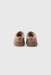 Pair of brown slip-on shoes with thick soles and woven trim, shown from the back on a white background.