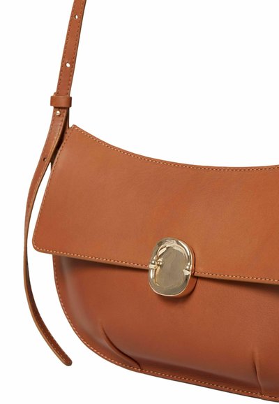 Bolso de cuero tan con forma curva, cierre de solapa y herrajes metálicos. Presenta detalles de costura y una correa larga ajustable.