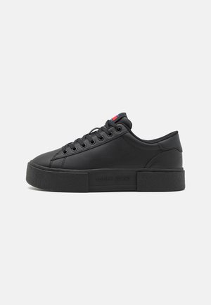 Czarny niskoprofilowy sneaker z grubą podeszwą, sznurowanym designem i małym czerwono-biało-niebieskim detalem flagi na języku, tłoczony "Tommy Jeans" po boku.