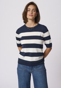 Pull en jersey à rayures bleu marine et blanches, à manches courtes, avec un col rond, une texture lisse et une coupe ajustée, associé à un jean bleu.