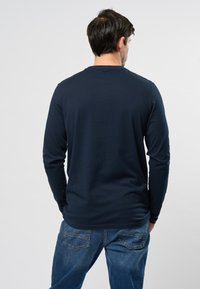Maglietta a maniche lunghe blu navy con scollatura a girocollo, realizzata in tessuto morbido. Indossata con jeans azzurri chiari, che mostrano un taglio rilassato e una superficie liscia.