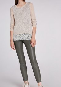 Beige lange mouw trui met een luipaardpatroon, over een groenachtige bloemenprint zoom heen gedragen, gecombineerd met strakke donkergroene leren broeken.