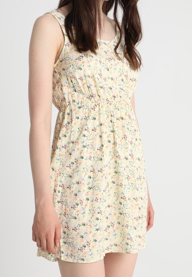 Robe imprimée florale en tissu jaune avec des fines bretelles, taille froncée et une texture légère et fluide. Présente de petites fleurs multicolores.