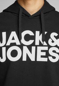 Black hoodie featuring a large white "JACK & JONES" print. The fabric is smooth with a relaxed fit and adjustable drawstrings at the hood.