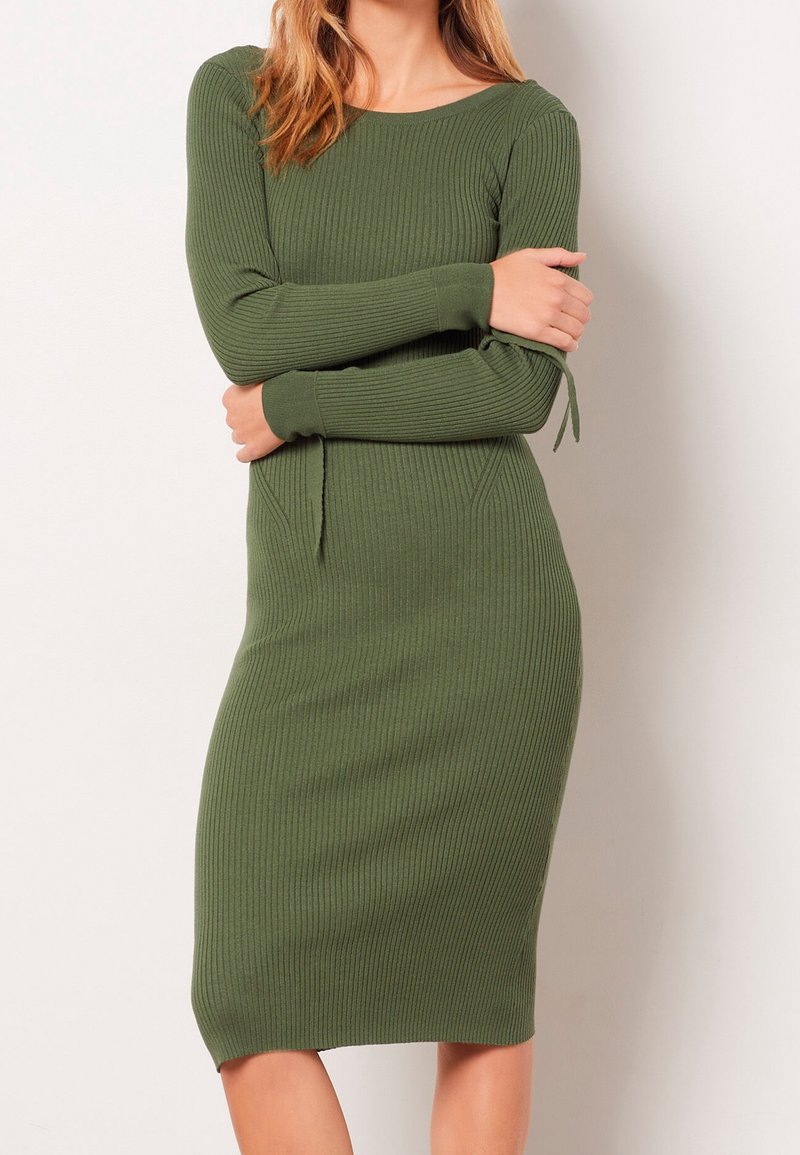 Ribbad stickad klänning i olivgrön med långa ärmar, har en båtformad halsringning och sidofästen vid ärmsluten. Slank passform och knälång.