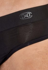 Schwarze Unterwäsche mit einem strukturierten Bund, der ein silbernes Logo trägt. Das Material wirkt glatt und hat ein tailliertes Design.