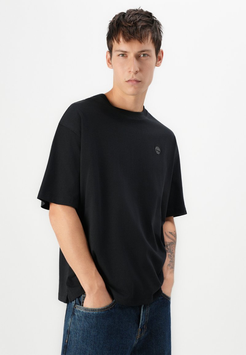 Czarna bawełniana koszulka z okrągłym dekoltem i krótkimi rękawami. Posiada małe logo na piersi oraz luźny krój.