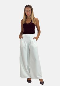 Pantalon blanc à jambes larges avec plis et poches, associé à un haut sans manches bordeaux. Le tissu semble lisse et léger.