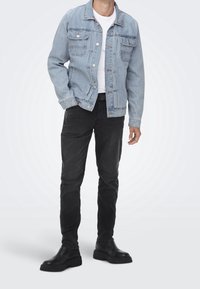 Ljusblå denimjacka med knappstängning och två bröstfickor, ihop med svarta slim-fit byxor och svarta ankelstövlar.