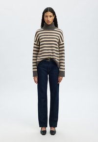 Gestreifter Rollkragenpullover in Hellbraun und Dunkelgrau, kombiniert mit dunkelblauen, geraden Jeans und schwarzen Ballerinas. Dezenter Rippstoff.