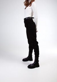 Pantalons noirs fuselés associés à un haut côtelé blanc. Le modèle porte des bottines noires avec un accent argenté brillant et une ceinture sombre.