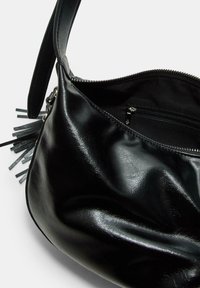 Schwarze Lederhandtasche mit glänzender Oberfläche, ausgestattet mit einem Reißverschluss, innerem Fach und Fransenverzierung an der Seite.