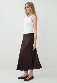 Top sans manches blanc associé à une jupe midi en satin marron et des ballerines tissées noires. Tissu lisse, corsage ajusté et design de jupe fluide.