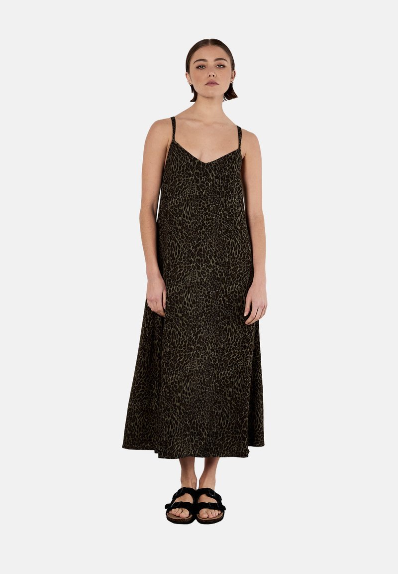Maxime dress with thin straps in dark green fabric featuring a leopard print pattern. Black sandals with thick straps on the model's feet.