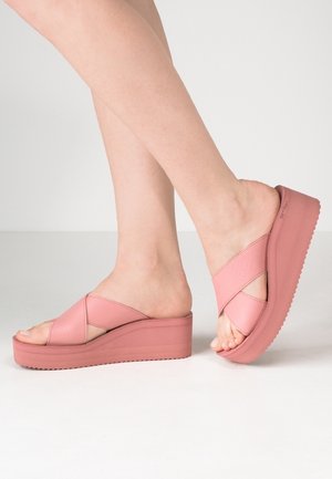 Pink kilehælssandaler med krydsede remme, der har en tekstureret overdel og en glat, solid sål. Forhøjet platform for ekstra højde og komfort.