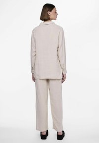 Camisa de lino suelta de color beige claro, con cuello, mangas largas y una textura sutil, combinada con pantalones anchos a juego.