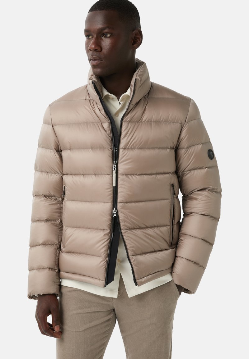 Beige pufferjakke med lynlås, stående krave og vandret quiltet design. Har sidelommer og et logo på ærmet.