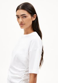 Weißes Kurzarm-T-Shirt mit Rundhalsausschnitt und seitlichen Raffungselementen, aus weichem Stoff mit glatter Textur.