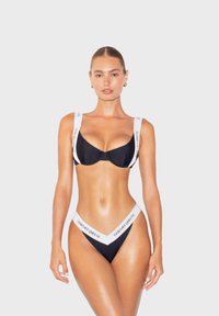 Černé bikini s bílými značkovými popruhy, s podprsenkovým vrškem a vysokým spodním dílem. Hladká textura, minimalistický design, důraz na nastavitelnost.