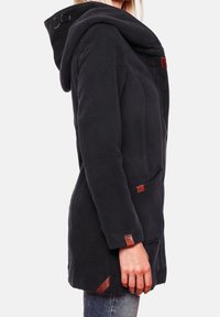 Giacca in pile nero con cappuccio spazioso, tasche laterali e dettagli in pelle. Presenta un design aderente e tessuto strutturato per il calore.