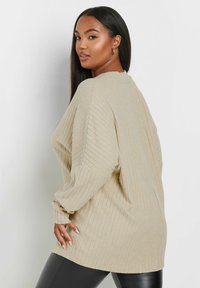 Överdimensionerad beige ribbad tröja med långa ärmar, rund halsringning och textilstruktur. Kombineras med svarta åtsittande leggings.