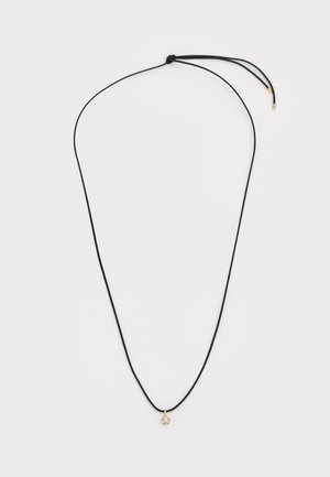 Collar de cuerda negra con un pequeño colgante dorado que tiene una piedra transparente. La cuerda es ajustable con un nudo en la parte superior.