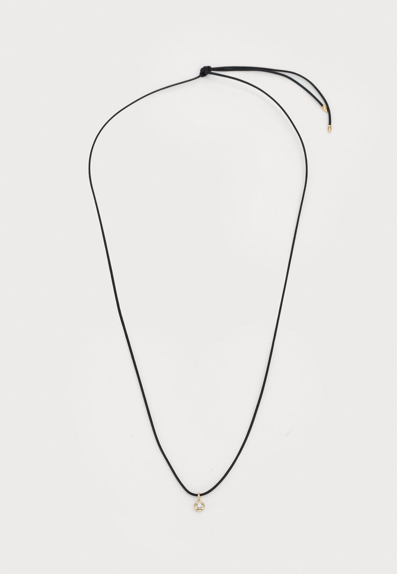 Collana in corda nera con un piccolo pendente dorato con una pietra trasparente. La corda è regolabile con un nodo in cima.