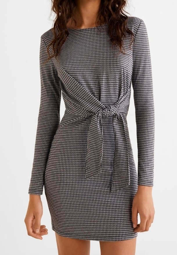 Femme portant une robe cintrée à manches longues à motif pied-de-poule avec un nœud à la taille devant et un col rond.