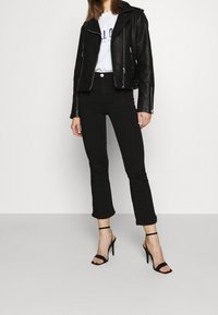 Chaqueta de cuero negro de motorista sobre una camiseta gráfica blanca, combinada con jeans negros de campana y sandalias de tacón alto negras con tiras.
