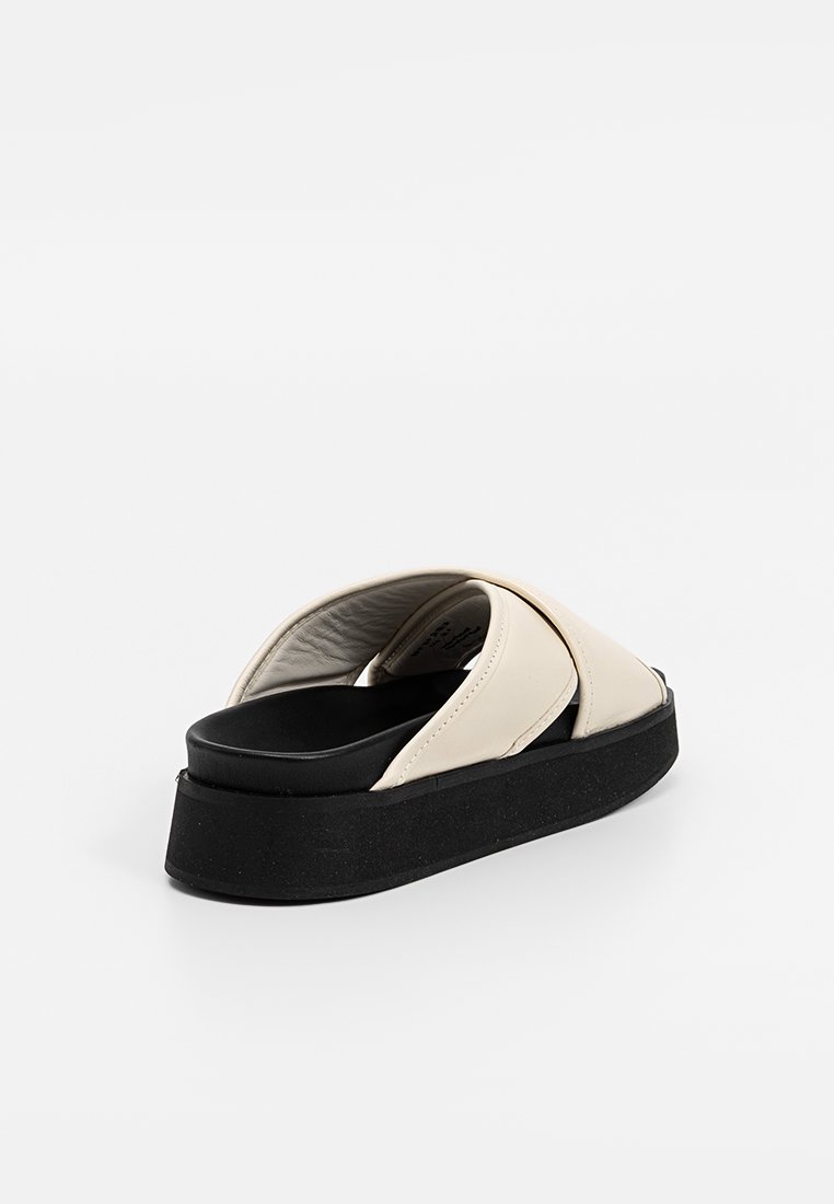 Sandales en cuir blanc à semelle en caoutchouc noir épais, avec un design de lanières croisées larges et une texture lisse sur le dessus.
