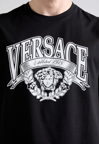Juodas medvilninis marškinėliai su centrinėmis baltomis grafikomis, vaizduojančiomis klasikinį biustą, apsuptą gėlių akcentų ir žodžiu „VERSACE“ viršuje.