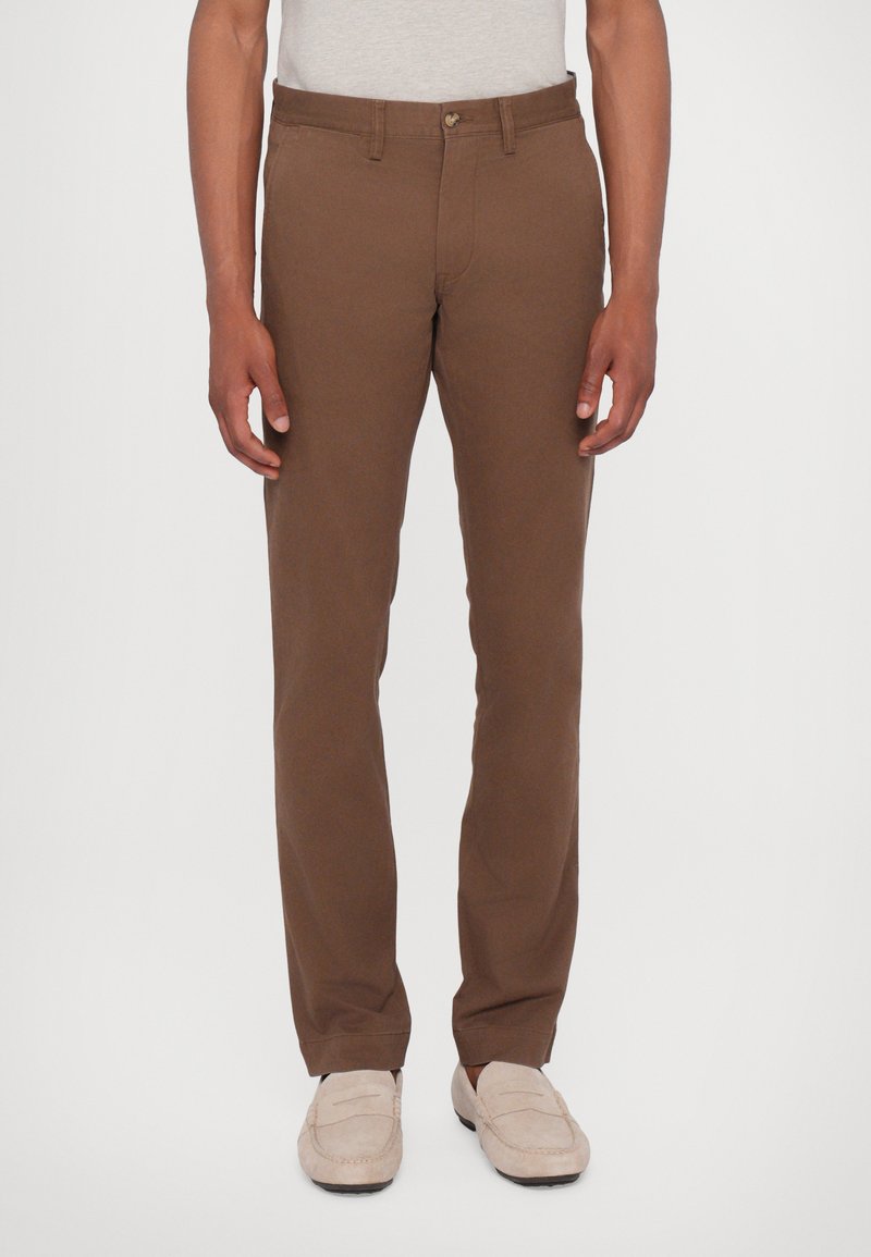 Pantaloni di cotone marroni con un design a gamba dritta, dotati di chiusura frontale con bottone e tasche laterali. Tessuto liscio senza motivi visibili.