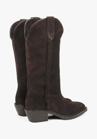 Brązowe zamszowe kowbojki z lekko spiczastym czubkiem, niskim, piętą o ograniczonej wysokości oraz falbaniastym detalem szwu biegnącym wzdłuż tyłu.