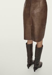 Jupe crayon en cuir marron avec un motif crocodile, associée à des bottes en cuir marron montantes et ajustées. Texture douce et design épuré.